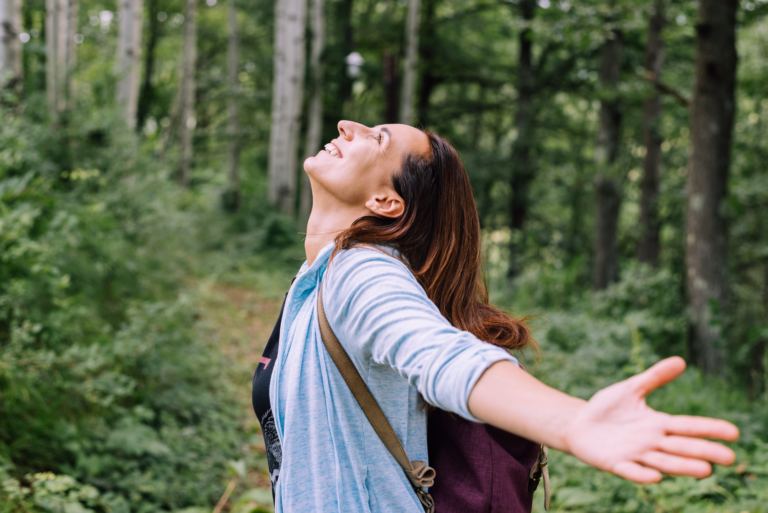 Woman enjoying nature with open arms on a forest trail, representing relaxation and mindfulness in forest bathing.