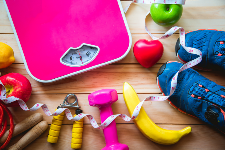 Pink scale with fitness gear and healthy foods.